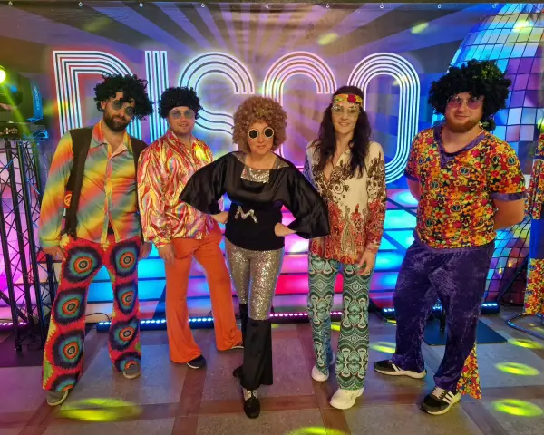 Pięć osób w kolorowych strojach disco z lat 70. na tle napisu "DISCO".