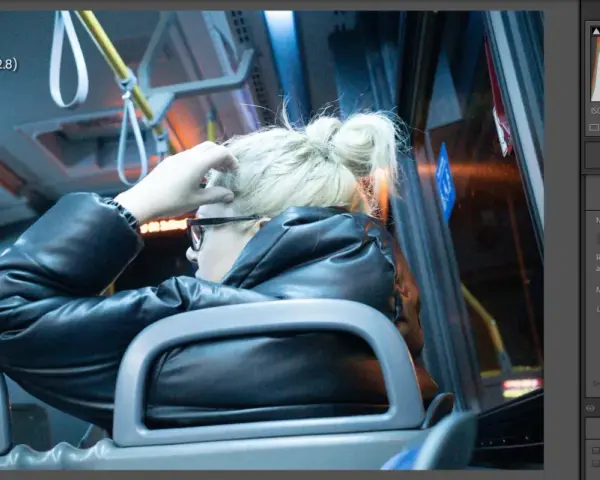 Kobieta w czarnej kurtce siedzi w autobusie, poprawiając włosy. Widać suwaki redukcji szumów w programie do edycji zdjęć.
