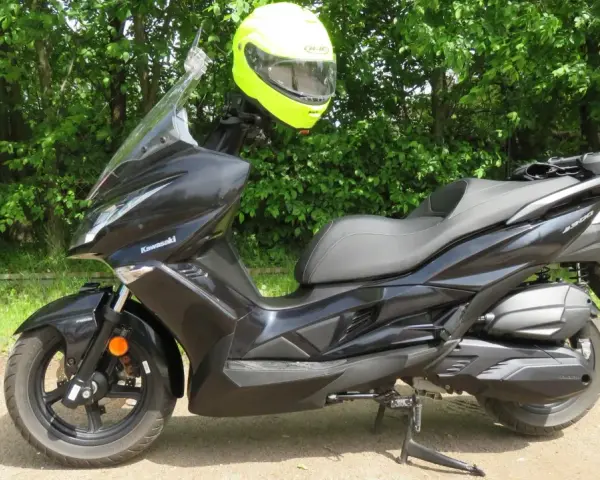 Czarny skuter Kawasaki J300 z jaskrawożółtym kaskiem zawieszonym na kierownicy, gotowy do jazdy w słoneczny dzień.