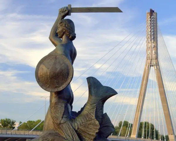 Syrenka Warszawska z mieczem i tarczą, symbol legendy o syrence warszawskiej, na tle nowoczesnego mostu.