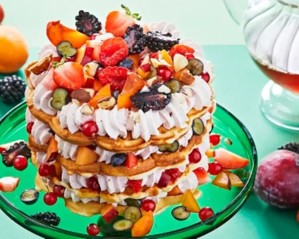 Eine beeindruckende Waffeltorte mit Erdbeeren und Mascarpone, geschichtet mit frischen Beeren und Früchten, auf einem grünen Teller.