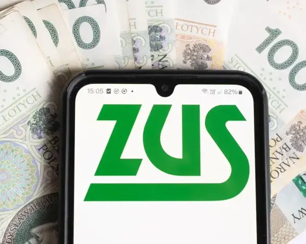 Telefon z logo ZUS na tle polskich banknotów 100 zł.