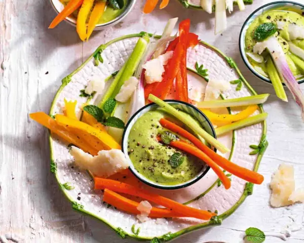 Deliziosi antipasti vegetariani: bastoncini di carote, peperoni e sedano con salsa verde cremosa, guarniti con scaglie di formaggio e menta.