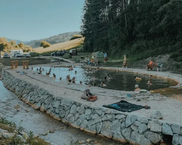 Relaks w dzikich gorących źródłach Słowacja. Ludzie kąpią się w naturalnym basenie otoczonym kamieniami, w tle góry i las.