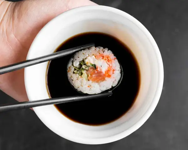 Pałeczkami zanurzam sushi w sosie do sajgonek. Widać kawałek łososia i ryż.