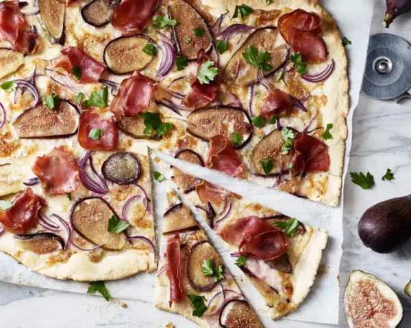 Ein köstlicher Flammkuchen mit Feigen, Schinken und roten Zwiebeln, garniert mit Petersilie.