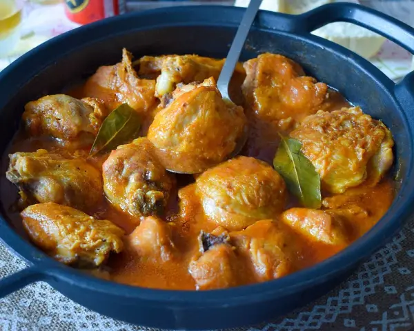 Sabroso pollo a la cerveza en cazuela negra, con salsa naranja y hojas de laurel.