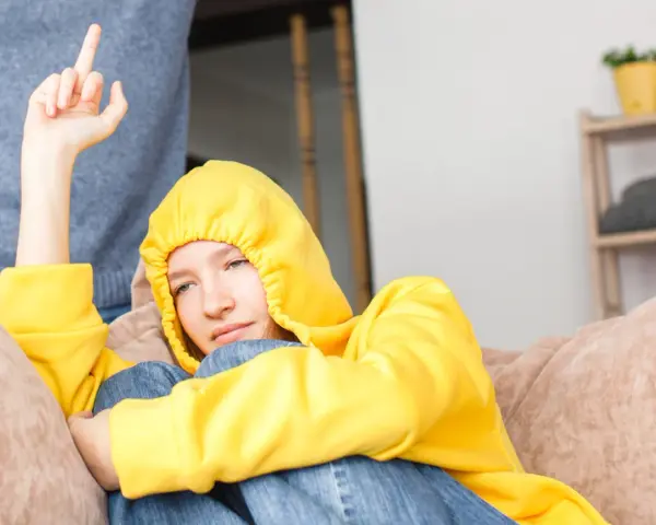 Ein Teenager in gelbem Hoodie zeigt seiner Mutter den Mittelfinger. Er hat keinen Respekt vor ihr.