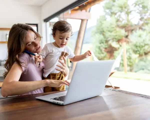 Als alleinerziehende Mutter jongliert sie Arbeit und Kind. Sie telefoniert, während sie ihr Kleinkind hält und am Laptop tippt.