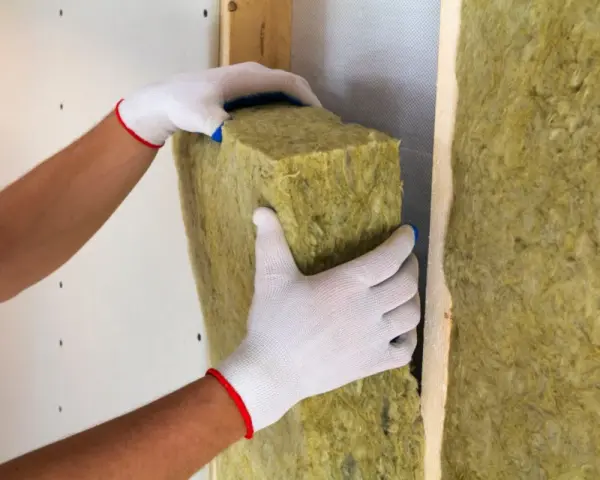 Mani guantate posizionano un pannello isolante, creando un cappotto interno o esterno per una parete.