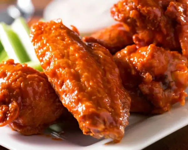 Alitas de pollo en freidora de aire, cubiertas de salsa picante, servidas con bastones de apio crujientes. ¡Un aperitivo irresistible!