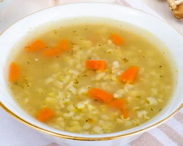 Aromaticzna zupa na rosole z makaronem i marchewką, podana w białej miseczce ze złotym rantem.