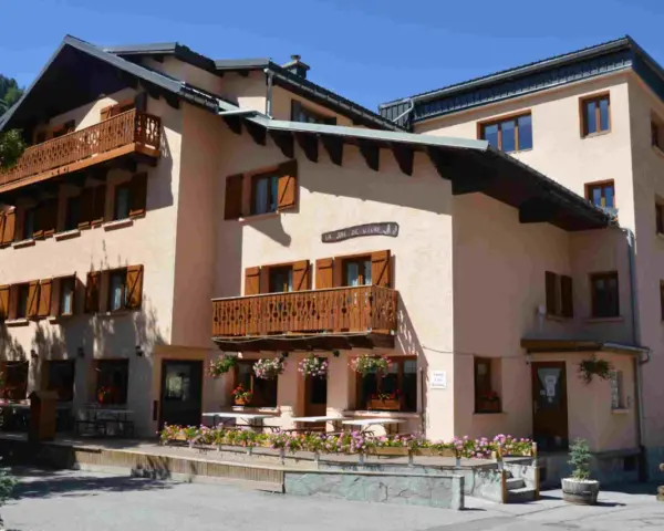 Bâtiment de style alpin avec balcons en bois et volets marrons, fleuri. Une enseigne "La Joie de Vivre" suggère une ambiance de colonie en Haute-Savoie.