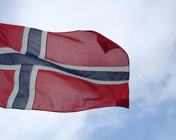 Flaga Norwegii powiewa na wietrze na tle błękitnego nieba z chmurami.