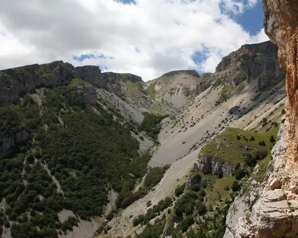 Un sentiero serpeggia tra montagne rocciose e vegetazione rigogliosa, un'avventura estiva al passo lanciano.