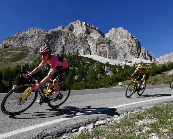 Cyclist in pink jersey, likely the winner of the Giro d'Italia, climbs a mountain road with a dramatic rocky peak behind.