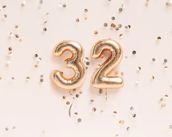 Złote balony z cyframi 3 i 2, otoczone konfetti. To już 32 tydzień ciąży, który to miesiąc?