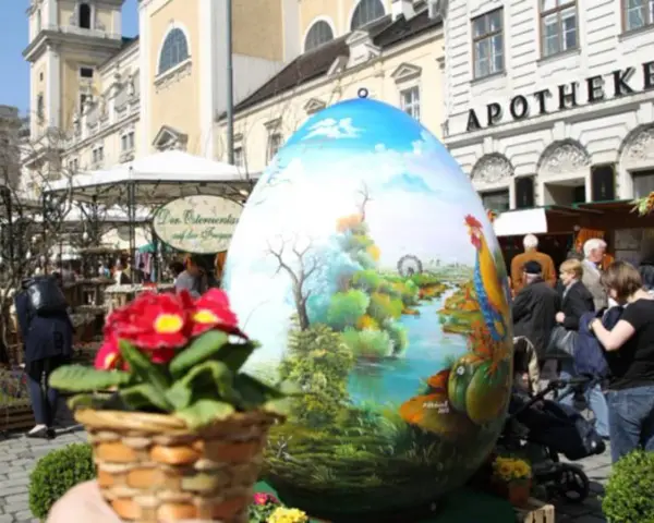 Großes, bemaltes Ei mit Frühlingslandschaft und Hahn, ein Osterbrunnen, der erklärt, warum ist Ostern immer wann anders.