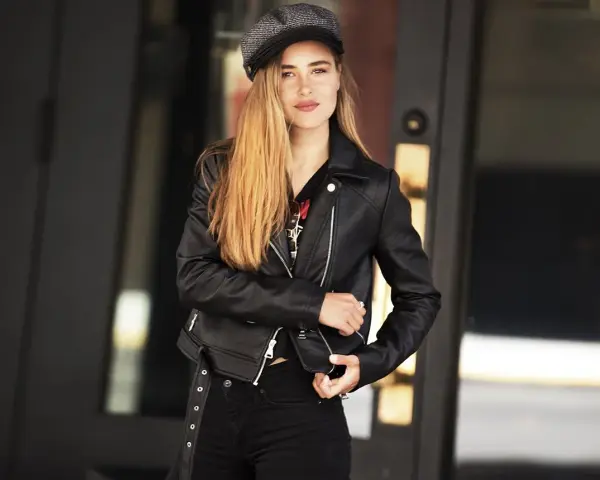 Dziewczyna w czarnej ramonesce i czapce, emanująca pewnością siebie w stylu glam rock.
