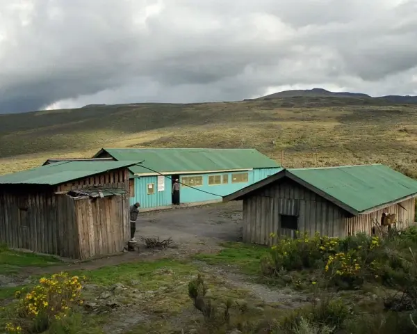 Proste chatki z zielonymi dachami na tle surowego krajobrazu u podnóża góry Mt Kenya.