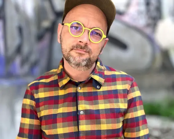 Filip Springer w okularach i koszuli w kratę, na tle graffiti.