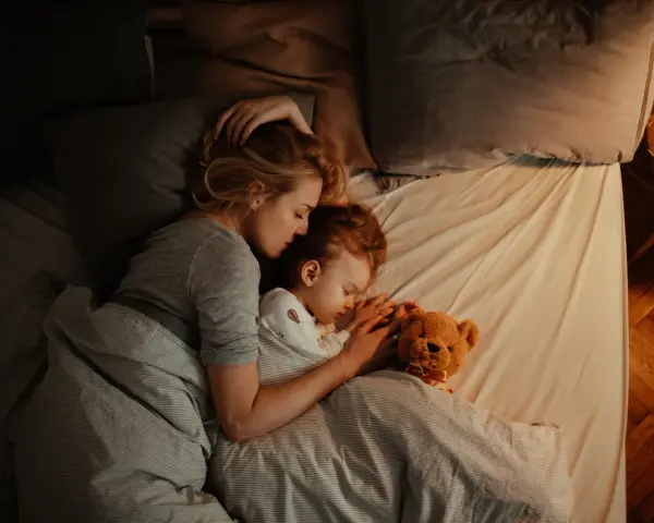 Mutter und Kind schlafen eng umschlungen. Ab wann Babys bewusst kuscheln, zeigt diese Szene der Geborgenheit.