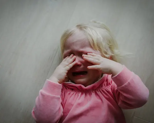 Małe dziecko płacze, zasłaniając oczy rękami. Wygląda, jakby dziecko uderzało głową o ścianę z frustracji.