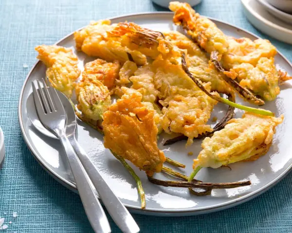 Piatto di fiori di zucca in pastella dorati e croccanti, serviti con sale grosso e posate.