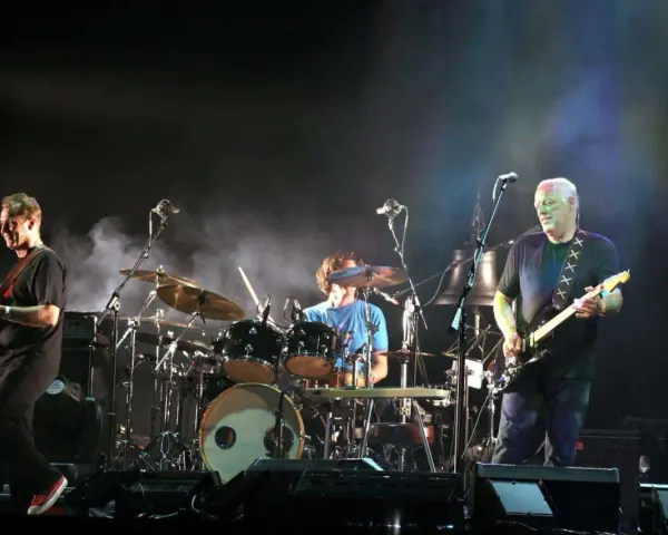 Les membres de Pink Floyd sur scène, David Gilmour à la guitare, Nick Mason à la batterie, et un autre musicien.