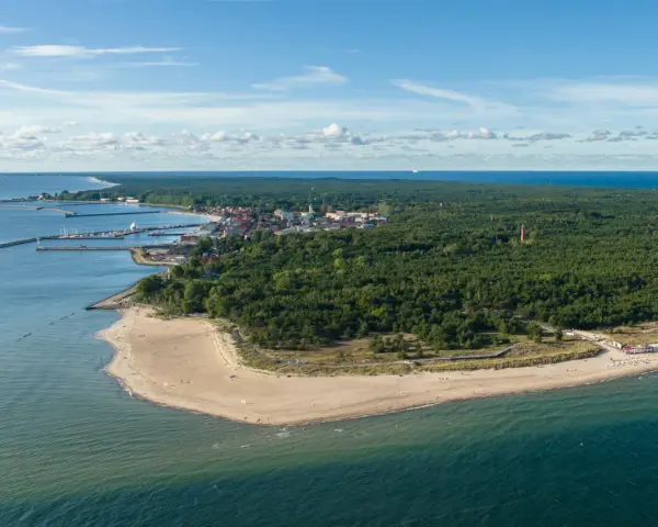 Widok na zatokę pucką z lotu ptaka. Widać piaszczystą plażę, las sosnowy, miasteczko z portem i latarnię morską.