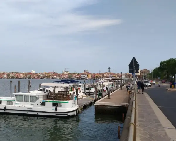 Un vaporetto attracca a Chioggia, con la città sullo sfondo e una strada trafficata.