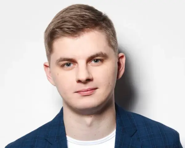 Młody mężczyzna w niebieskiej marynarce w kratę, gotowy do występu. Polski stand up w jego wykonaniu to gwarancja dobrej zabawy.