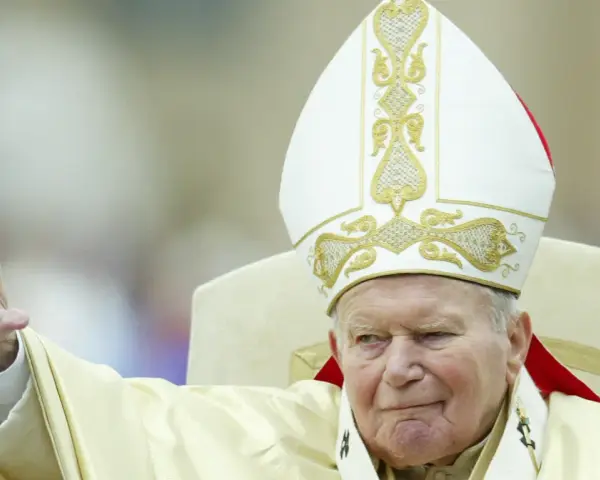 Papież Jan Paweł II w białej mitrze z haftem, pozdrawia wiernych. Jego dłoń z pierścieniem jest uniesiona. Codzienna modlitwa do św. Jana Pawła II.