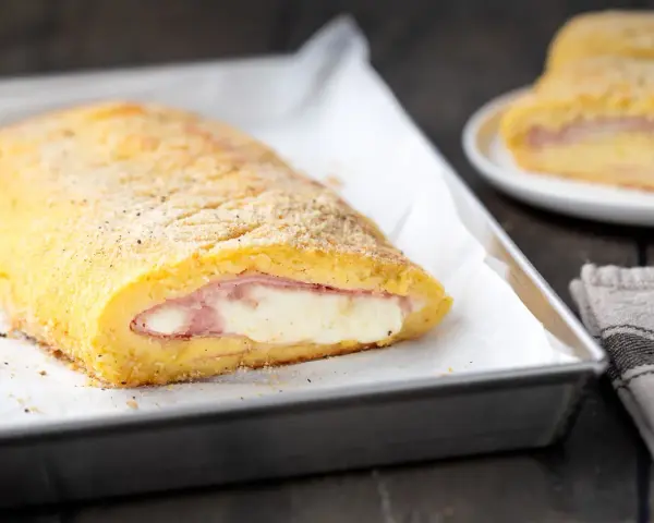 Rotolo dorato di polpettone di patate ripieno di prosciutto e formaggio filante, pronto per essere gustato.