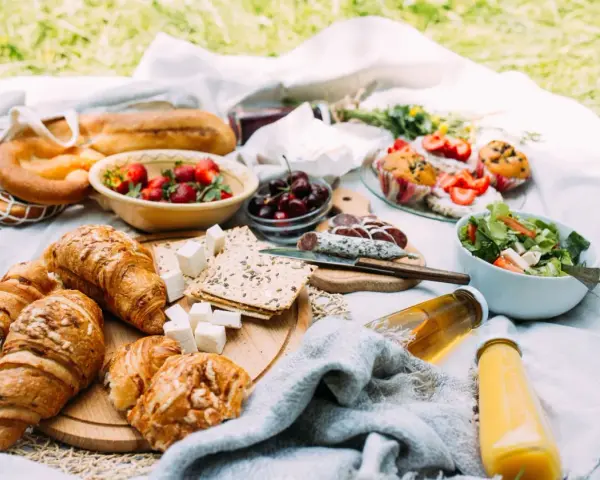 Pyszne jedzenie na piknik: świeże pieczywo, owoce, sałatka, sery i napoje.
