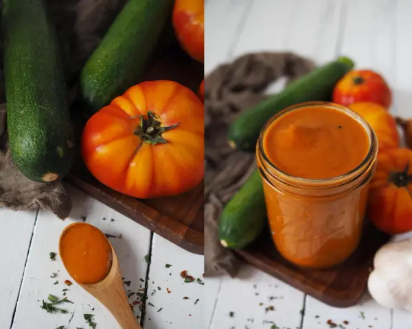 Zucchini-Ketchup in einem Glas, daneben frische Zucchini, Tomaten und Knoblauch. Ein Löffel mit dem Ketchup liegt daneben.