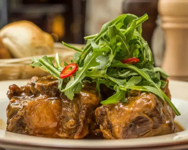 Delicioso rabo de toro en salsa, coronado con rúcula fresca y rodajas de chile. Una receta que conquista paladares.