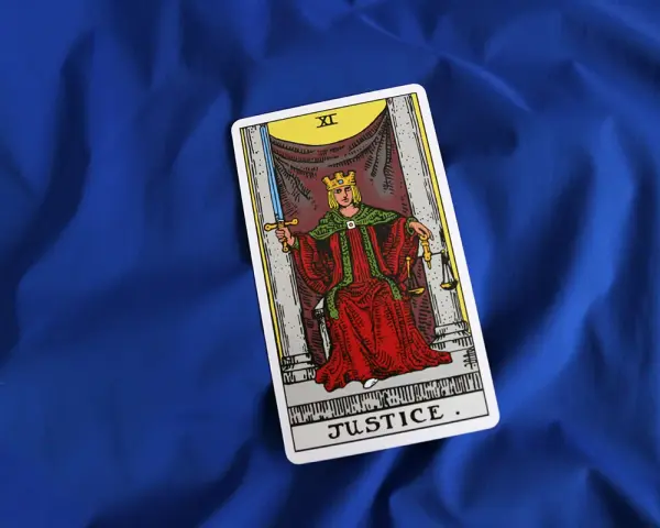 Karta XI Sprawiedliwość z talii tarot na niebieskim tle. Królowa z mieczem i wagą symbolizuje równowagę i prawdę.