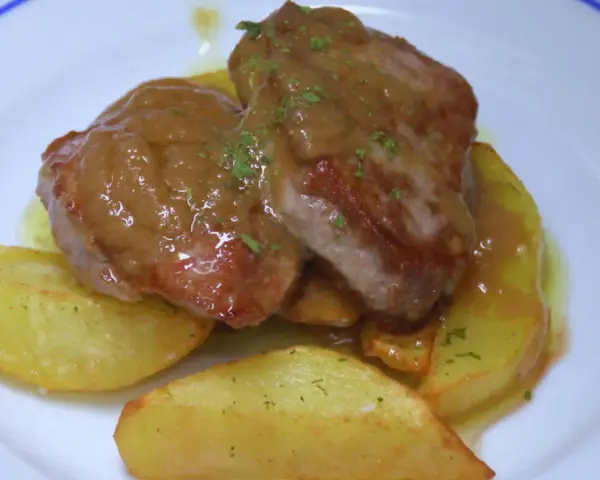 Solomillo jugoso con salsa de whisky sobre patatas gajo en un plato blanco.