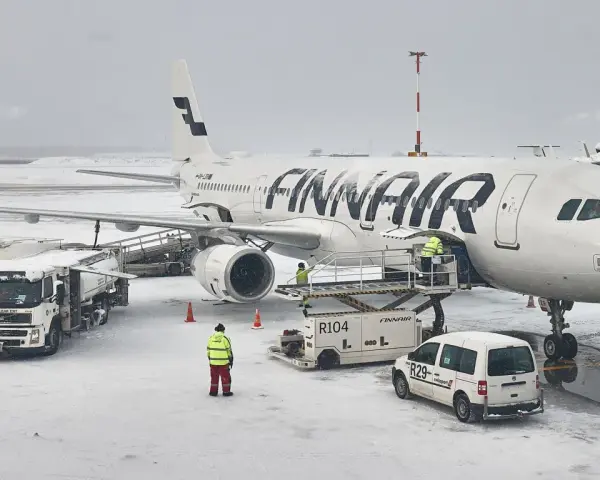 Samolot Finnair na lotnisku w śnieżny dzień. Pracownicy obsługi naziemnej przygotowują samolot do lotu. Czy do Finlandii można lecieć na dowód?