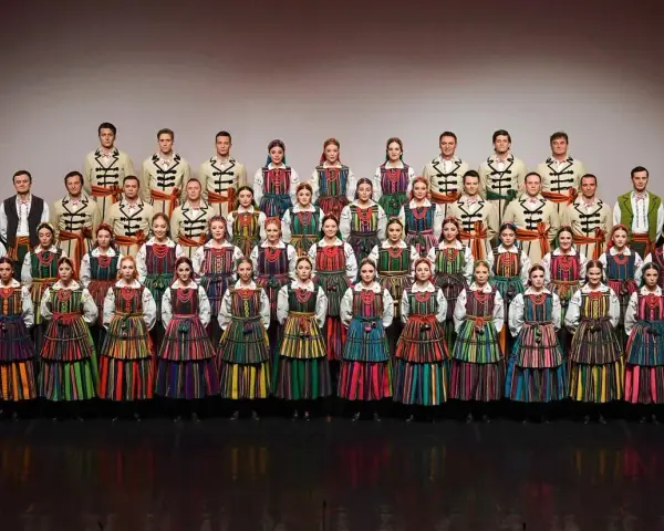 Zespół w barwnych strojach ludowych, prezentujący mazowieckie piosenki ludowe.