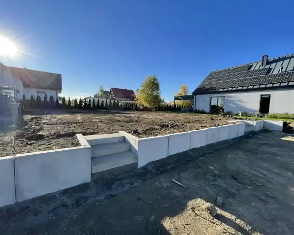 Nowe schody i betonowy murek to co zamiast muru oporowego, otaczają plac budowy domu z panelami słonecznymi.