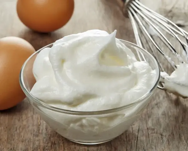 Zwei Eier und ein Schneebesen neben einer Schüssel mit luftigem Eischnee, der nicht fest wird.
