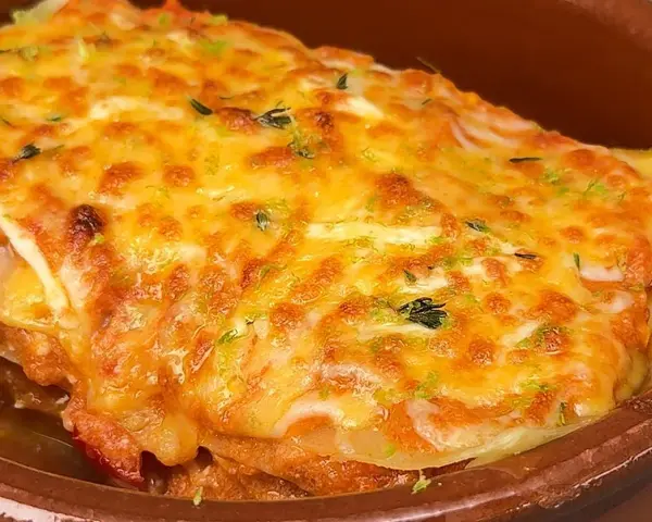Deliciosa lasaña de atún gratinada con queso dorado y hierbas frescas, servida en una cazuela de barro.