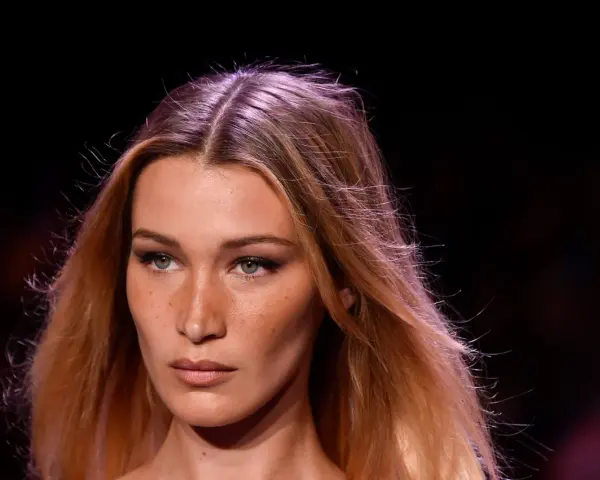 Primo piano di una modella con capelli biondi mossi e occhi verdi penetranti. La sua espressione è enigmatica, quasi a chiedersi chi è la donna più bella del mondo.