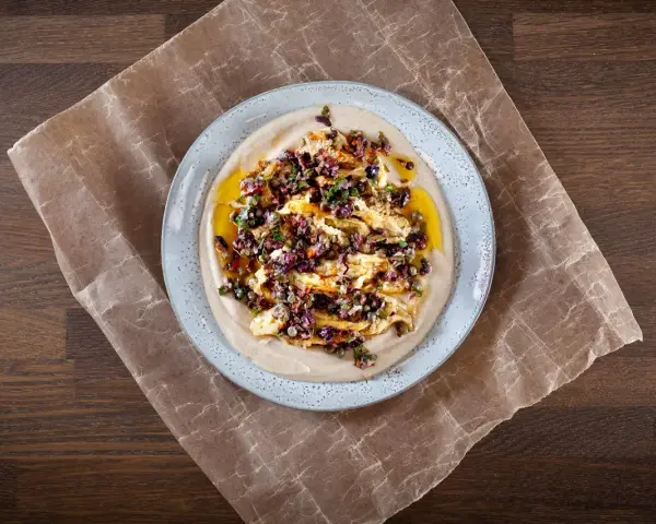 En krämig aubergine i ugn serveras på en bädd av hummus, toppad med en smakrik blandning av oliver, kapris och örter.