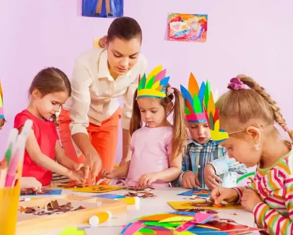Nauczycielka pomaga dzieciom w tworzeniu pióropuszy. Jedno z dzieci, 4-latek, nie chce się bawić z dziećmi, ale skupia się na pracy.