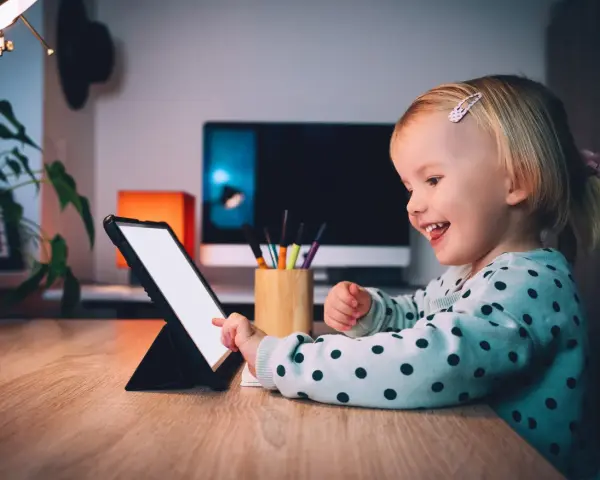 Uśmiechnięta dziewczynka ogląda ulubionych youtuberów dla dzieci na tablecie.