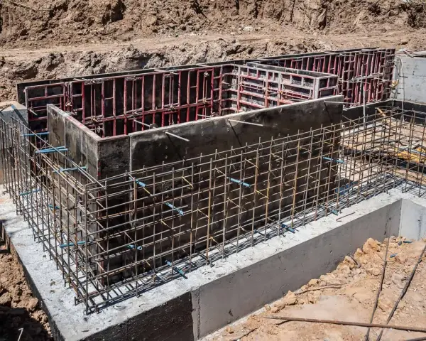 Siatka zbrojeniowa otacza betonowe szalunki, tworząc solidne zbrojenie ściany fundamentowej.