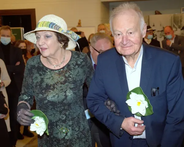 Ewa Dałkowska z synem Ksawerym, elegancko ubrani, z kwiatami w dłoniach, podczas uroczystości.